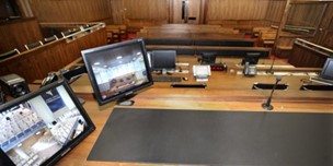 Remote-Hearing-Image An image of a meeting room with 2 monitors on a desk receiving a remote hearing call